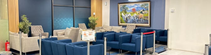 The seating area in Saphire Lounge Halim Perdanakusuma features comfortable chairs and a decorative painting, providing a relaxing space for travelers.