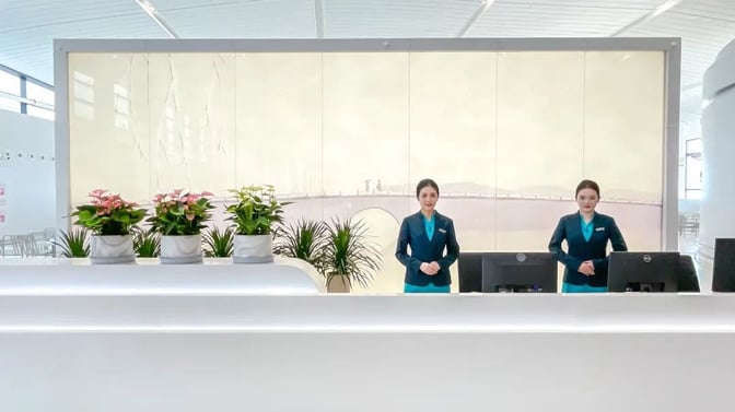 The reception area at VIP Lounge V25 in Hangzhou Xiaoshan International Airport features a staffed desk with decorative plants.