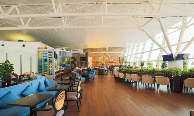 The SH Premium Lounge at Noi Bai International Airport features diverse seating options, a self-serve food area, and large windows with airport views.