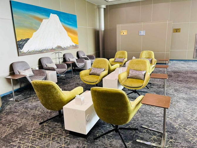 The seating area in Hayyak Lounge at Bisha Domestic Airport features comfortable chairs with side tables and a large wall painting.