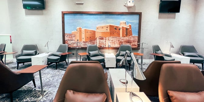 The seating area in Hayyak Lounge at Hail International Airport features comfortable chairs, side tables, and a large wall mural.