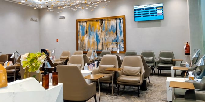 The seating area in Hayyak Lounge at Prince Naif bin Abdulaziz International Airport features comfortable chairs with individual tables and a flight information screen.