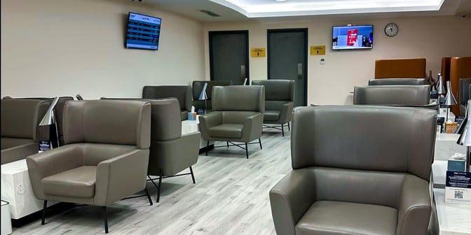 The seating area at Hayyak Lounge, Najran Regional Airport, features individual armchairs with side tables and wall-mounted flight information screens.