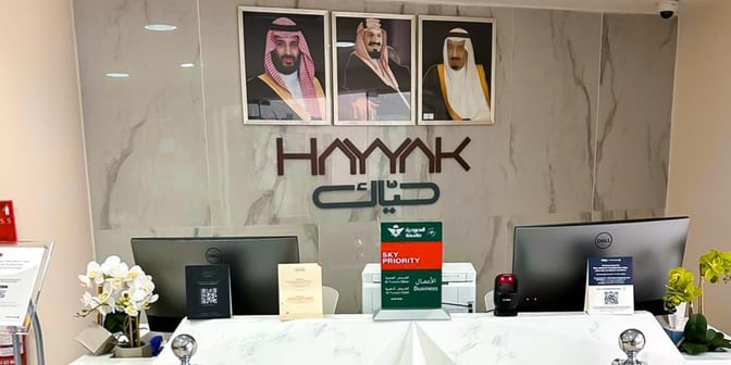 The reception area of Hayyak Lounge at Najran Regional Airport features a service desk with computers and informational signage.