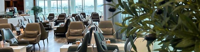 The Hayyak Lounge at Prince Sultan bin Abdul Aziz Airport features comfortable seating with tables, offering views of the airport through large windows.