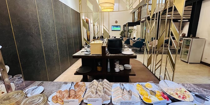 The UCB Imperial Lounge at Hazrat Shahjalal International Airport features a self-serve food area with sandwiches, fruits, and beverages.
