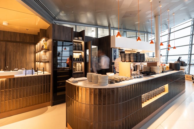 The OP Lounge by Aspire at Helsinki-Vantaa Airport features a self-serve food station with stacked plates and bowls for travelers.