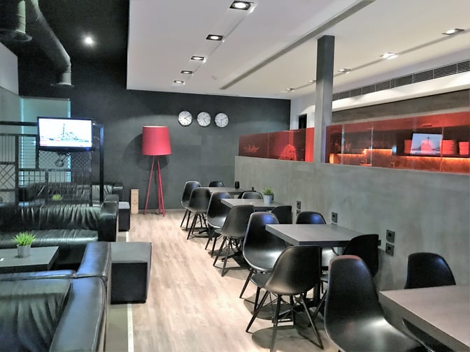 The Filoxenia Lounge at Heraklion International Airport features seating with tables and a television for passenger relaxation.