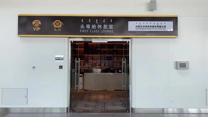 The entrance to the First Class Lounge at Hohhot Baita International Airport features a reception desk and bookshelves.