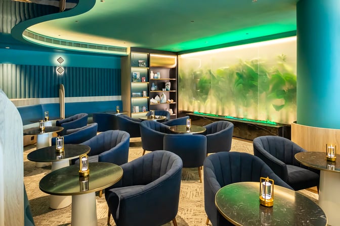 The seating area at Kyra Lounge, Hong Kong International Airport, features round tables with armchairs and decorative shelving.