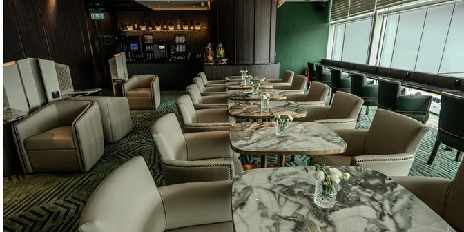 The seating area in Plaza Premium First lounge near Gate 35 at Hong Kong International Airport features marble tables and cushioned chairs.