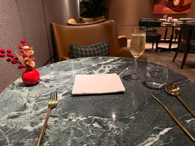 A dining table in the Plaza Premium First lounge at Hong Kong International Airport is set with cutlery, a glass of champagne, and a water glass.