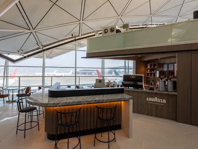The Plaza Premium Lounge near Gate 60 at Hong Kong International Airport features a Lavazza coffee bar with seating and tarmac views.