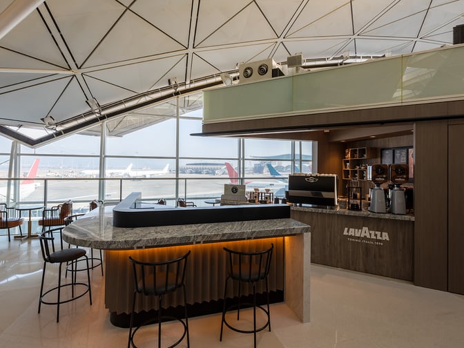 The Plaza Premium Lounge near Gate 60 at Hong Kong International Airport features a Lavazza coffee bar with seating and tarmac views.