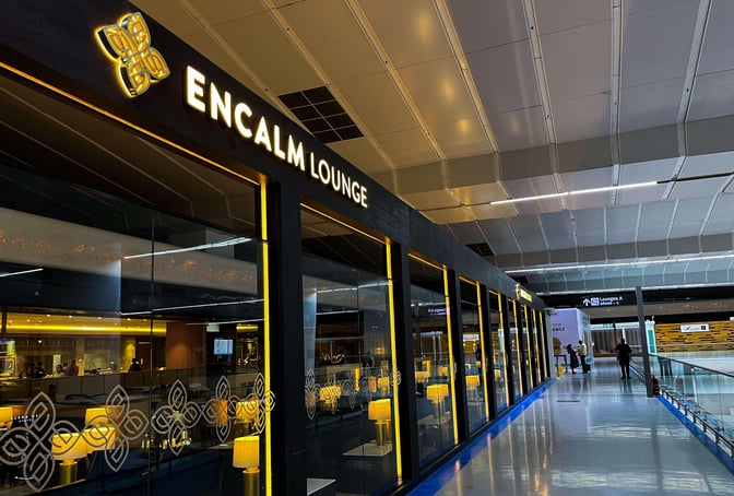 The Encalm Lounge entrance at Indira Gandhi International Airport features glass walls and is located along a main terminal walkway.