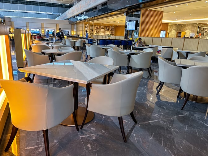 The seating area in Encalm Lounge at Indira Gandhi International Airport features tables and chairs for dining and relaxation.