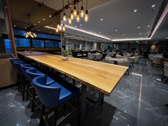 The Encalm Lounge at Indira Gandhi International Airport features a long communal table with bar seating and a spacious seating area.