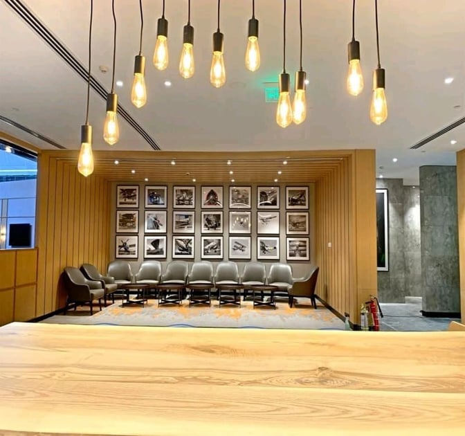 Seating area at Encalm Lounge, Indira Gandhi International Airport, features a row of chairs and framed aviation-themed photographs on the wall.