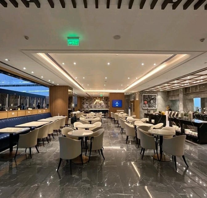 The Encalm Lounge at Indira Gandhi International Airport features a spacious seating area with tables and chairs for dining and relaxation.