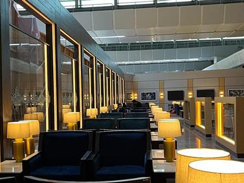 Seating area in Encalm Lounge at Indira Gandhi International Airport features rows of armchairs with side tables and lamps for traveler comfort.