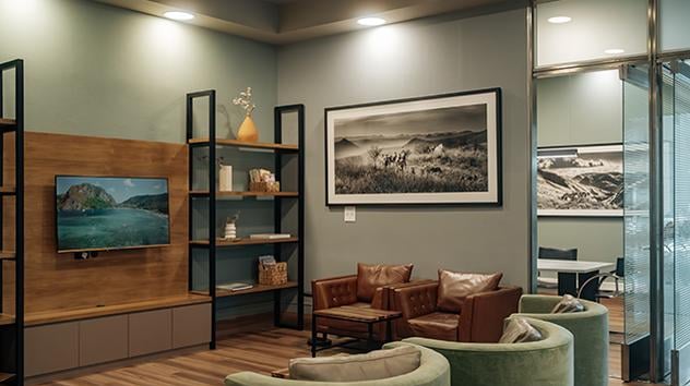 The lounge seating area at Cordoba by AMAE Lounge features comfortable chairs, a television, and bookshelves for relaxation and entertainment.
