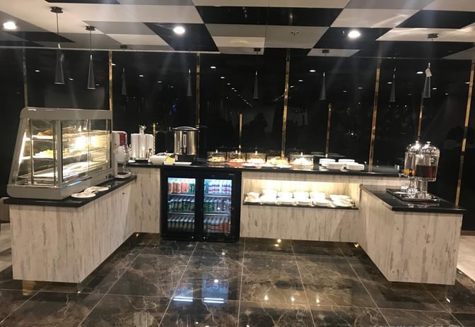 The food area in Islamabad International Airport's airline lounge features self-serve stations with snacks, beverages, and a refrigerated drinks section.