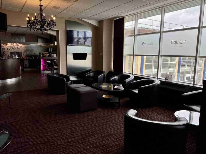 The Rendezvous Executive Lounge at Isle of Man Airport features comfortable seating with a view of the tarmac and a nearby bar area.