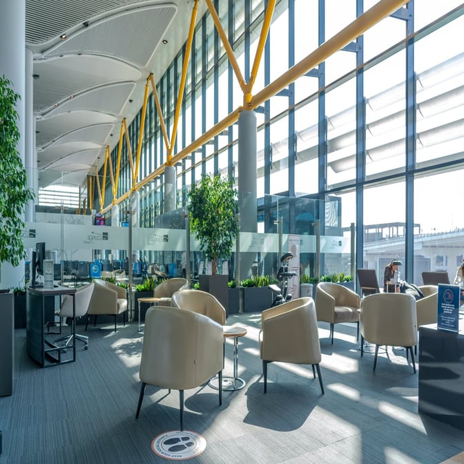 The IGA Lounge at Istanbul Airport features a seating area with armchairs and tables, offering views of the tarmac through large windows.