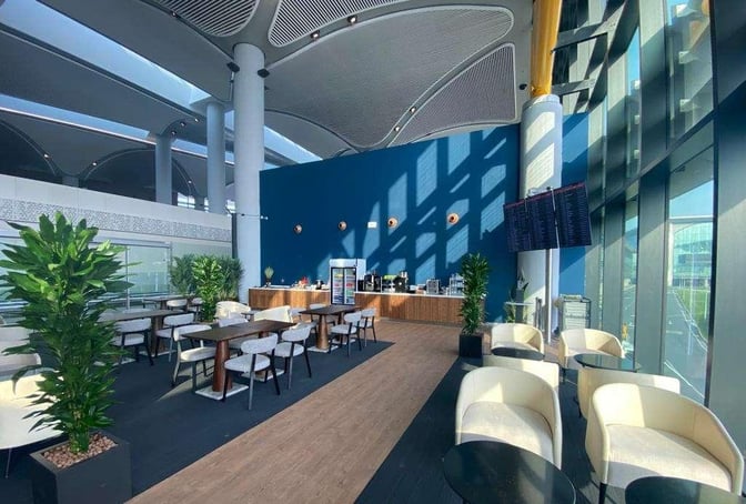 The IGA Pop Up Lounge at Istanbul Airport features a seating area with tables and chairs, adjacent to a self-serve refreshment counter.