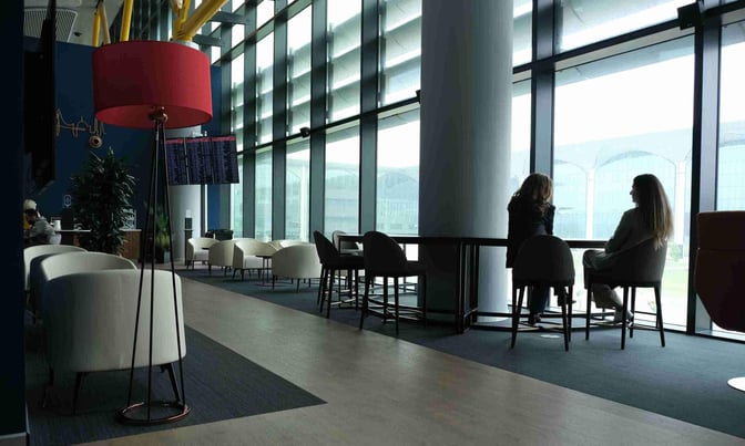 The IGA Pop Up Lounge at Istanbul Airport features seating areas with armchairs and tables, offering views of the airport through large windows.