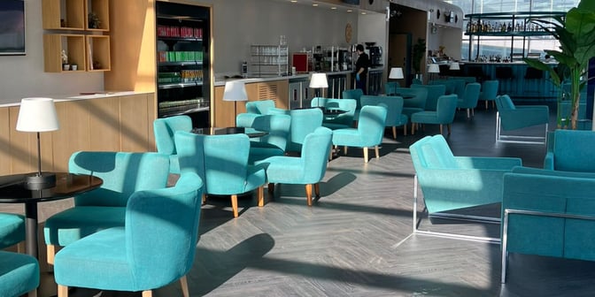 The Primeclass Lounge at Izmir Airport features a seating area with armchairs and tables, adjacent to a self-service beverage station.