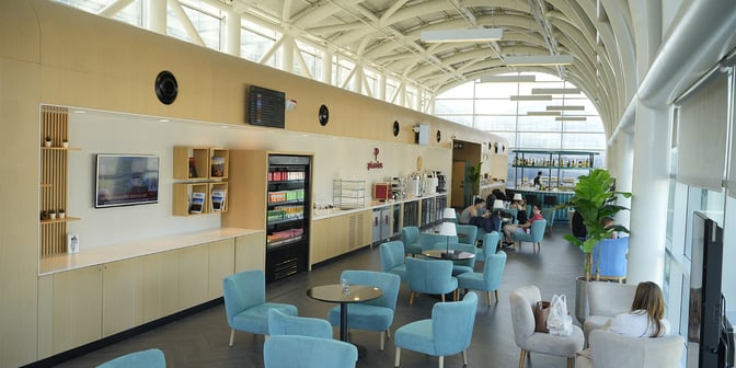 The Primeclass Lounge at Izmir Airport features a seating area with tables, a self-serve beverage station, and a bar.
