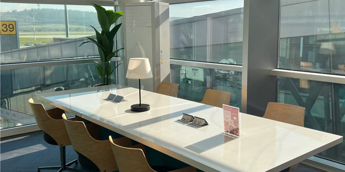 A seating area in the Primeclass Lounge at Izmir Airport features a long table with chairs, power outlets, and runway views.