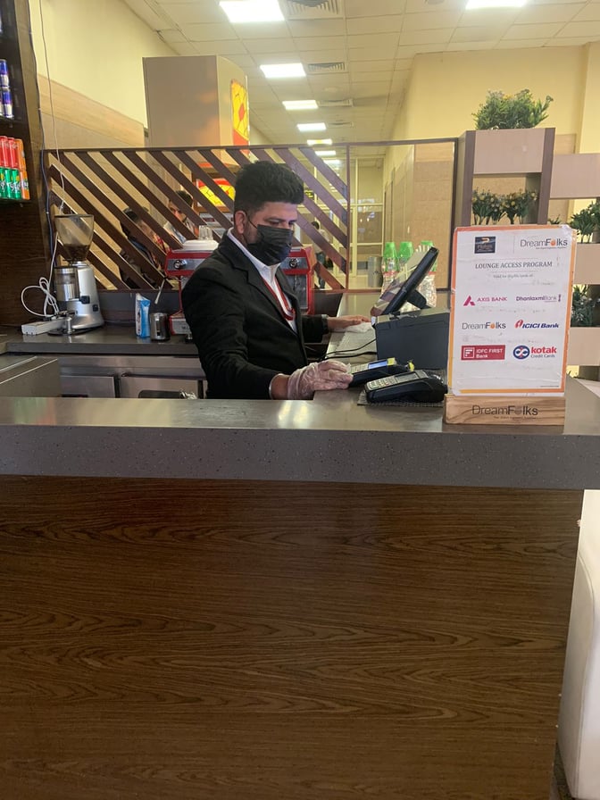 The reception area at Paahun The Executive Lounge, Jammu Airport, features a staff member managing check-ins and a lounge access program display.