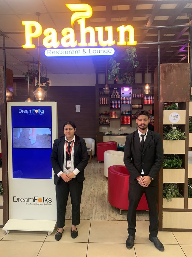 The entrance to Paahun Restaurant & Lounge at Jammu Airport features staff welcoming guests, with visible seating and a display screen.
