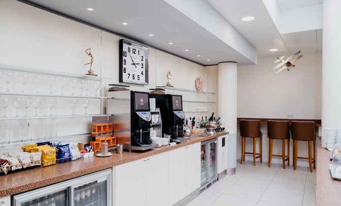 The Executive Lounge at Jersey Airport features a self-serve snack and beverage station with coffee machines, snacks, and bar seating.