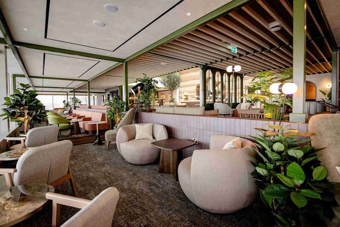 The No1 Lounge at Jersey Airport features a spacious seating area with various chairs and tables, surrounded by greenery.