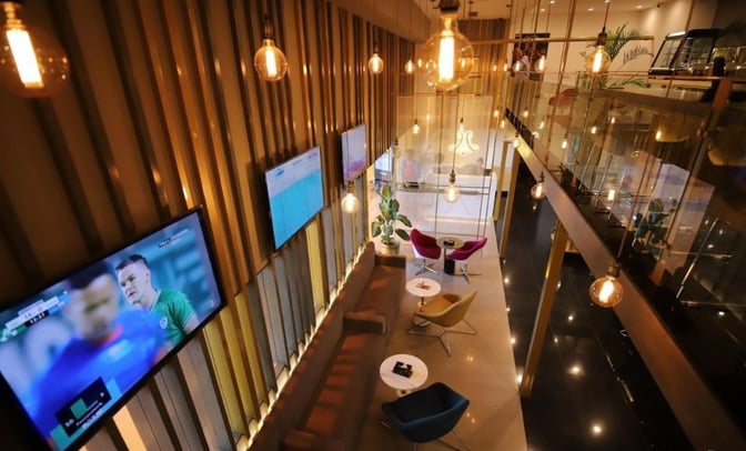 The Majestic Lounge at Jinnah International Airport features seating with tables, multiple televisions, and a view of the entrance area.
