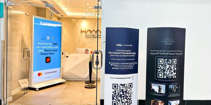 The entrance to Hayyak Lounge at King Abdullah bin Abdulaziz International Airport features promotional displays for meal offers and lounge access apps.