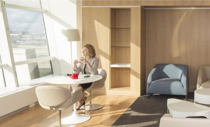 Seating area in the Air France Lounge at JFK Airport features round tables and chairs with views of the runway.