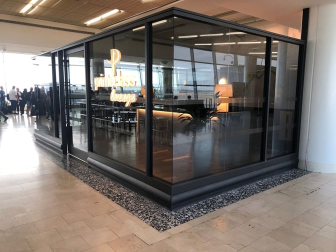 The Primeclass Lounge entrance at JFK Airport features glass walls and is located near a seating area with airport views.