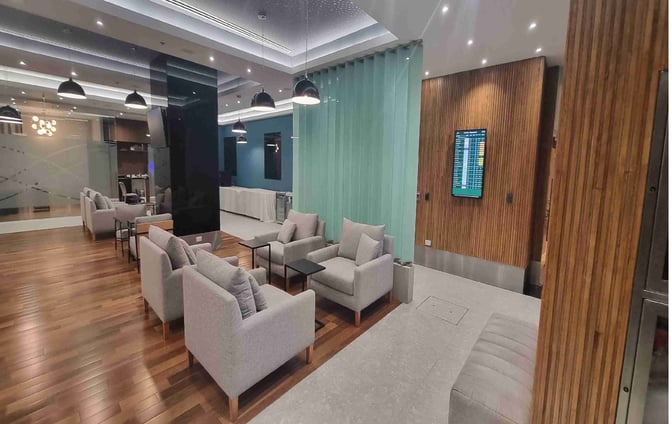 The AMAE Lounge at Aeroparque features comfortable seating areas with armchairs and tables, alongside a flight information display screen.
