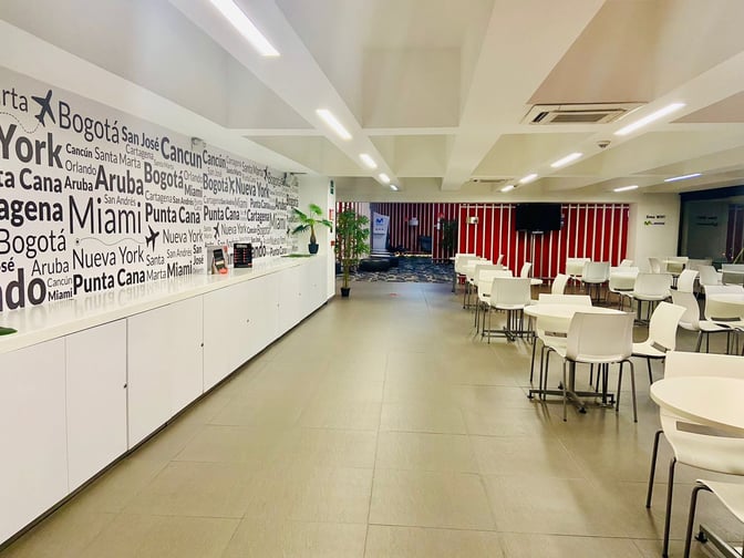 The Avianca Lounge at José María Córdova International Airport features a seating area with tables and chairs, adjacent to a wall with destination names.