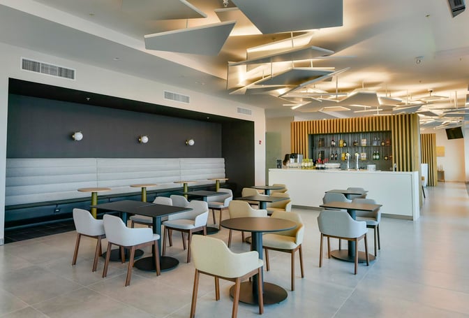 The BAC Credomatic lounge at Juan Santamaría International Airport features a seating area with tables and chairs adjacent to a bar.