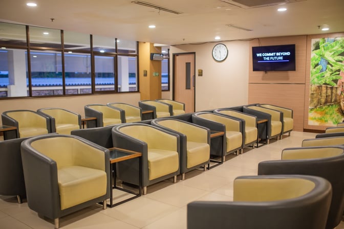 The seating area in Concordia Lounge at Juanda International Airport features rows of armchairs with side tables and a wall-mounted screen.