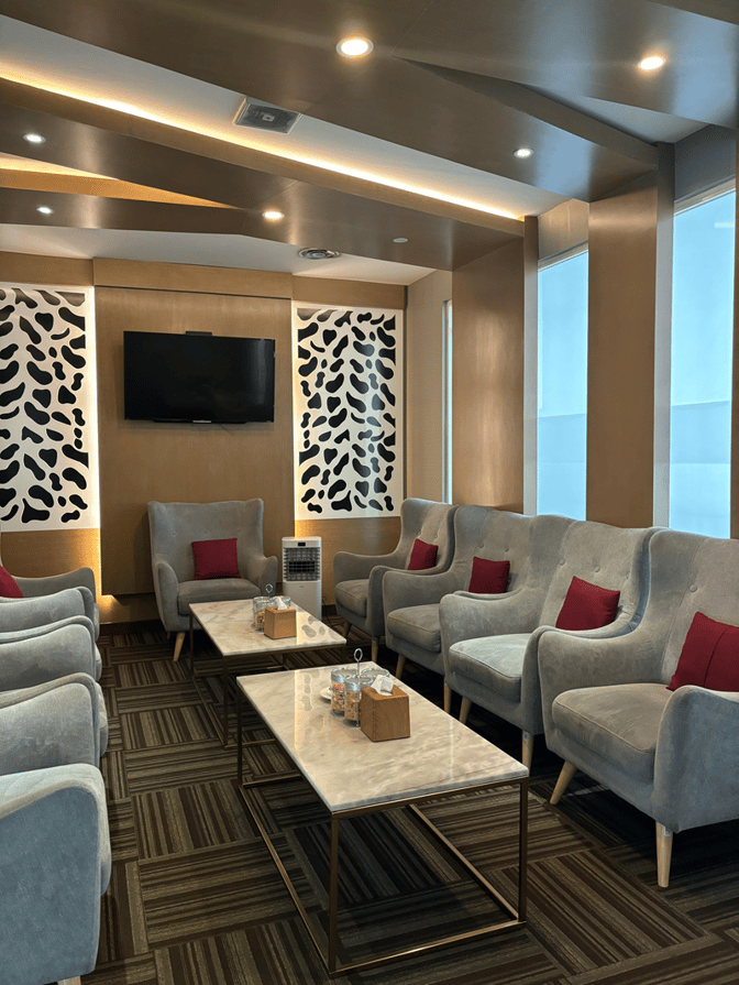 The seating area in Concordia Premier Lounge at Juanda International Airport features comfortable armchairs and tables with a wall-mounted TV.