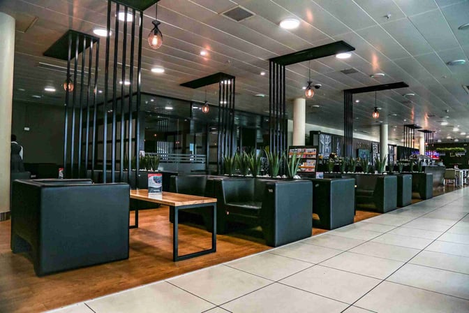 The CIP Lounge at Julius Nyerere International Airport features booth seating with tables and decorative plants, providing a comfortable waiting area.