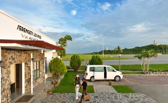 The Serengeti Lounge entrance at Julius Nyerere International Airport features a stone facade and is accessible via a paved walkway.