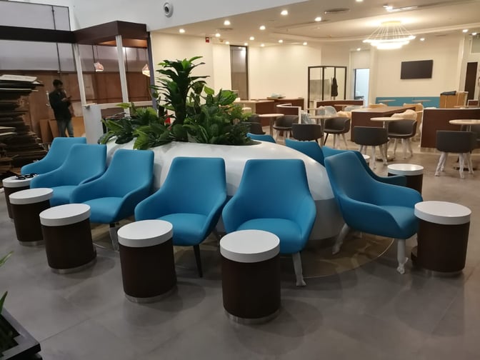 The seating area at Pearl Lounge, Kannur International Airport, features comfortable chairs and tables arranged around a central plant display.