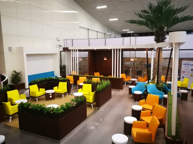 The seating area at Pearl Lounge, Kannur International Airport, features various chairs and tables surrounded by greenery for passenger relaxation.